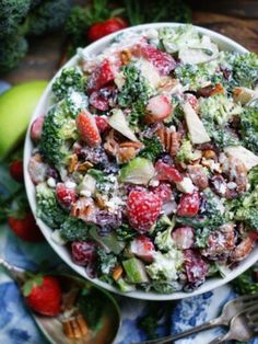 a white bowl filled with broccoli, strawberries and other food on top of a table