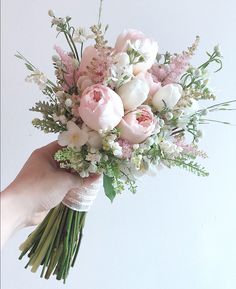 a person holding a bouquet of flowers in their hand with white and pink flowers on it