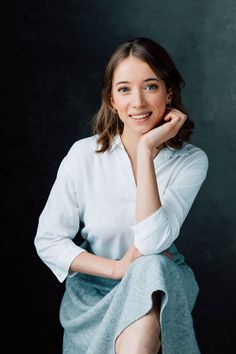 a woman sitting on top of a chair in front of a black background wearing a white shirt and blue skirt