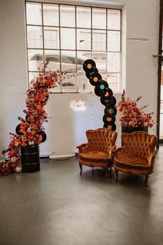 two old chairs sitting next to each other in front of a wall with flowers on it