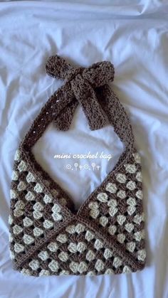 a crocheted purse is laying on a bed with white sheets and brown trim