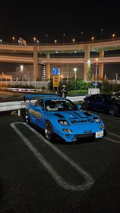 a blue car parked in a parking lot next to an overpass at night time