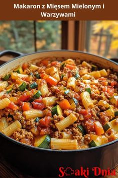 a skillet filled with pasta and meat on top of a wooden table next to a window