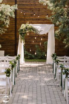 an outdoor ceremony with white chairs and greenery