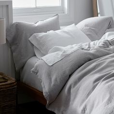 an unmade bed with white linens and pillows in front of a large window