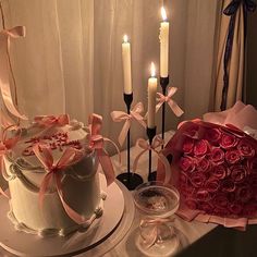 a table topped with two cakes covered in frosting and roses next to candles on top of each cake