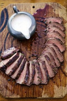 sliced meat on a wooden cutting board next to a small bowl of ranch dressing and a spoon