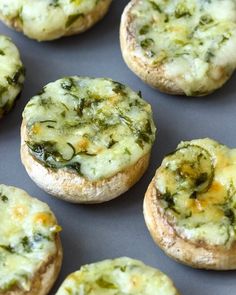 several small pizzas with cheese and spinach on them sitting on a baking sheet