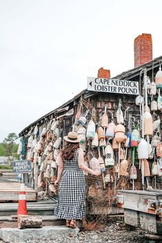 a woman standing in front of a store with lots of hats on it's roof