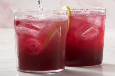 two glasses filled with red drinks sitting on top of a white counter next to each other