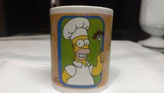 a coffee cup with the image of homer simpson holding a spatula in his hand