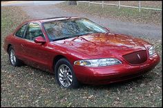 a red car parked on the side of a road in front of a tree and grass field