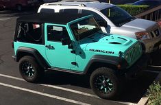 a blue jeep parked in a parking lot next to a silver truck and some bushes