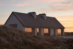 a white house sitting on top of a hill next to a grass covered hillside at sunset