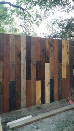 a fence made out of wooden planks in the yard with trees and grass behind it