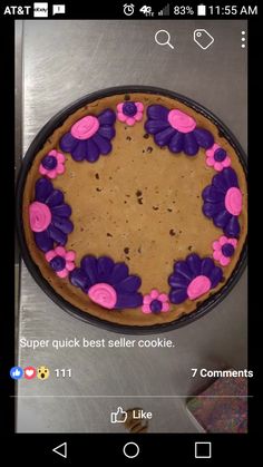 a cake with purple flowers on it sitting on top of a metal counter next to a cell phone