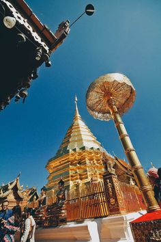 an umbrella stands in the foreground as people walk past it on a sunny day