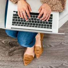 a woman is sitting on the floor with her laptop in her lap and she's wearing brown shoes