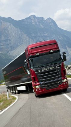 a red semi truck driving down the road with mountains in the backgrouund