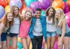 a group of young people standing next to each other with balloons in the air behind them