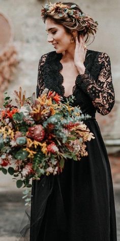 a woman in a black dress holding a bouquet and talking on the phone while wearing a flower crown