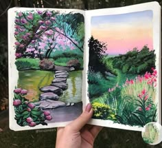 someone is holding an open book with watercolors on it and flowers in the background