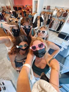 three women wearing goggles and masks in a clothing store looking at the camera while another woman takes a selfie with her phone