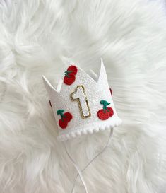 a white crown with red apples on it sitting on top of a fluffy white blanket