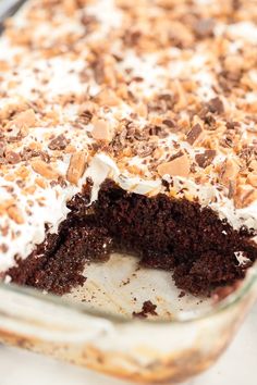 a chocolate cake with white frosting and chopped nuts on top is in a glass dish