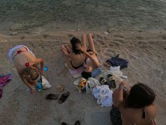 two women are sitting on the beach with their feet in the sand and one is covering her face