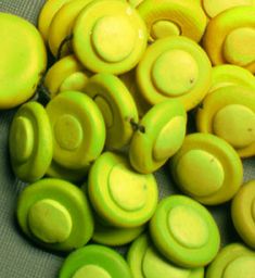 yellow and green buttons are sitting on a gray tablecloth, some have holes in them