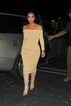 a woman in a tan dress and thigh high boots walking out of a car door