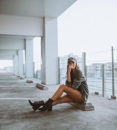 a woman is sitting on the ground talking on her cell phone while wearing black boots