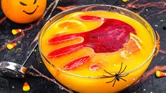 an orange drink in a glass with candy on the rim and halloween decorations around it