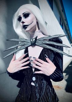 a woman with white hair and makeup holding scissors in front of her face while wearing a creepy costume