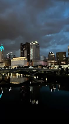 the city skyline is lit up at night with clouds in the sky and reflecting on the water