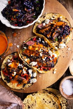 three tacos on a cutting board with salsa and tortillas next to it