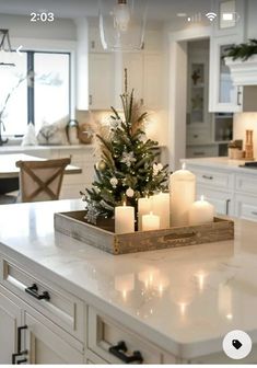 a christmas tree in a tray on top of a kitchen counter with candles and lights around it