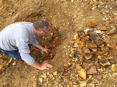 a man kneeling down next to a pile of wood on top of a dirt field