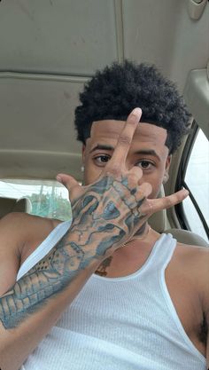 a man with tattoos on his arm making the peace sign while sitting in a car