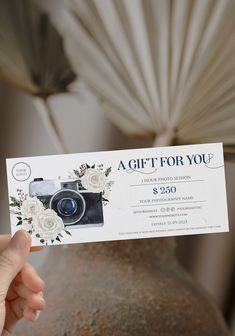 a person holding up a gift for you card in front of a vase with flowers