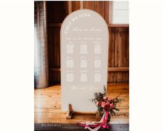 a wedding seating sign with flowers on the side and red ribbon tied to it's back