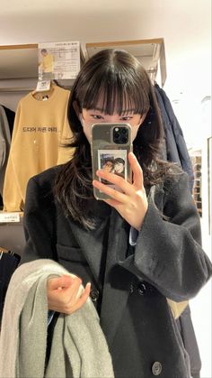 a woman taking a selfie with her cell phone in front of some clothing racks