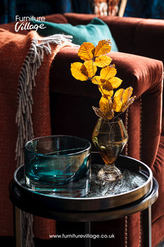 a glass vase filled with yellow flowers sitting on top of a table next to a bowl