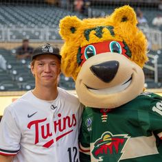 a man standing next to a mascot wearing a baseball uniform on top of a field