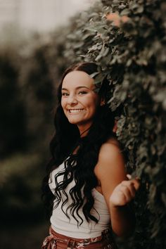 a woman standing next to a bush smiling at the camera