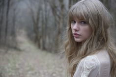 a woman with long blonde hair standing in the woods