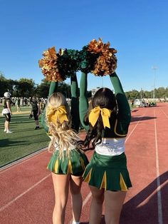 two cheerleaders holding up their pom poms in the air on a track