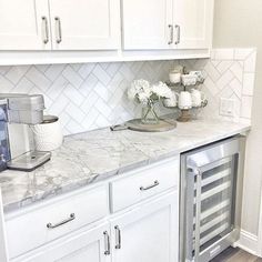 a white kitchen with marble counter tops and stainless steel appliance in the corner