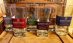 four glasses sitting on top of a wooden table in front of an old box with labels